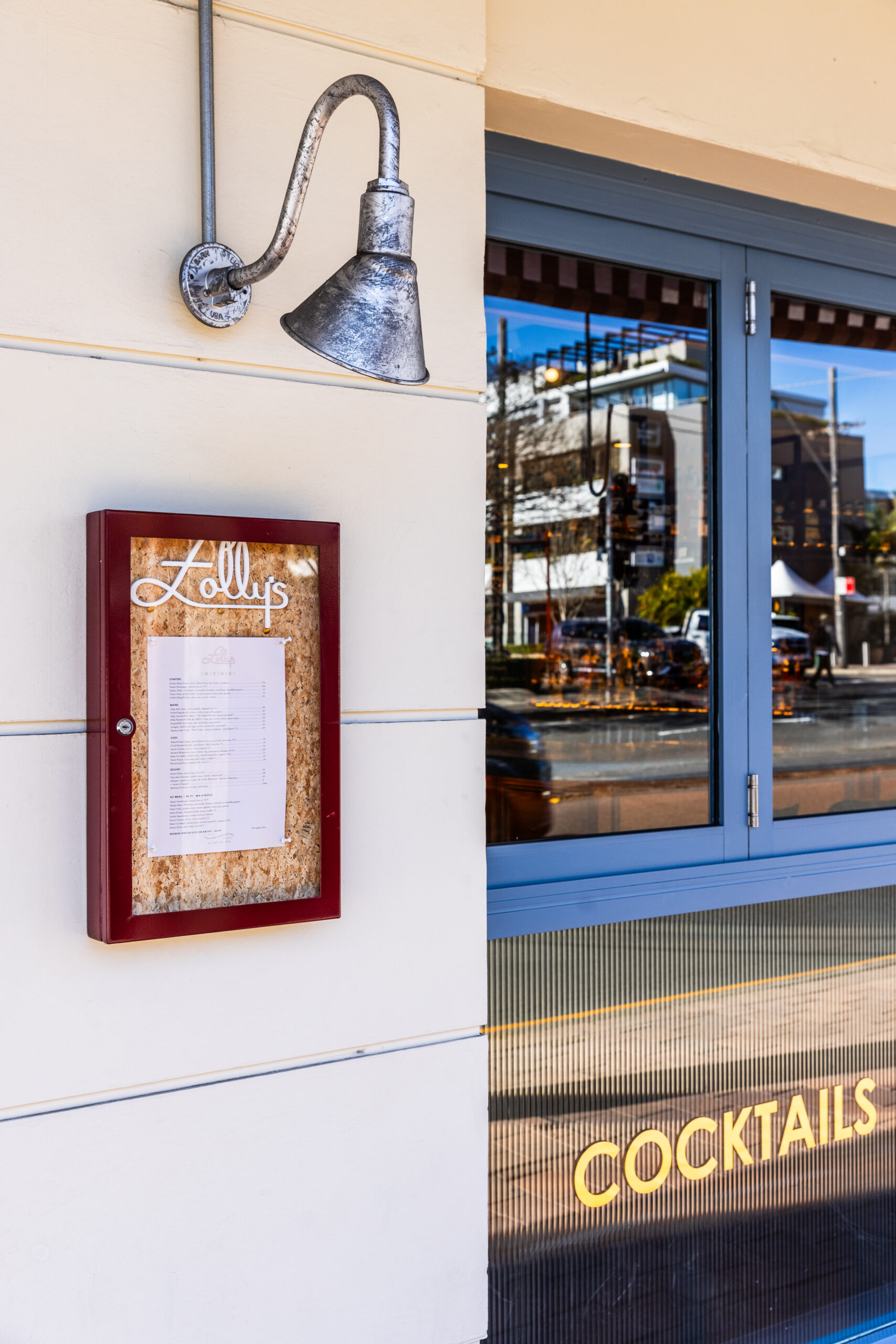 Exterior of Folly's bar and bistro, featuring menu in framed image and metal lamp above.